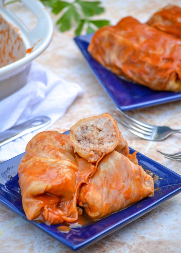 Rollos de col Rellenas de Halupki picantes se sirven en un plato cuadrado azul con una ramita de perejil y una espátula de plata al fondo