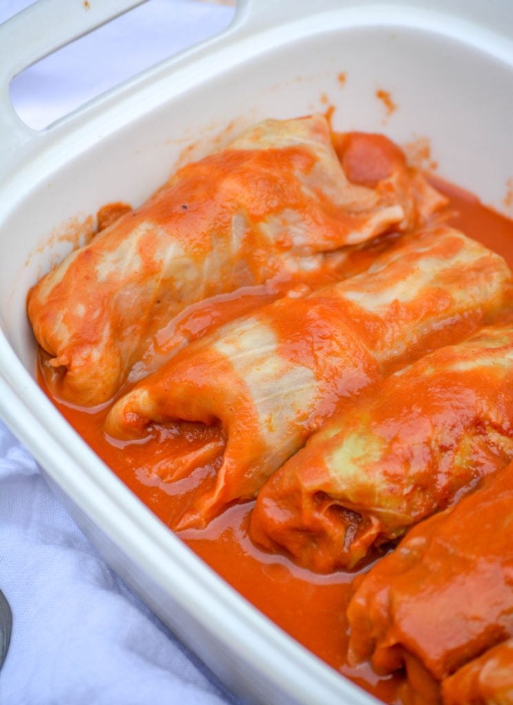 Halupki Stuffed Cabbage Rolls shown bathed in a vibrant red tomato sauce mixture in a deep casserole dish