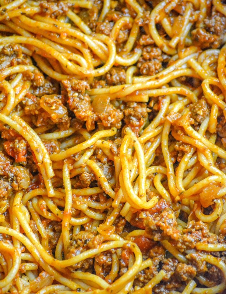 a close up of One Pot Spaghetti showing the saucy chunks of cooked ground beef and tomato & onion pieces