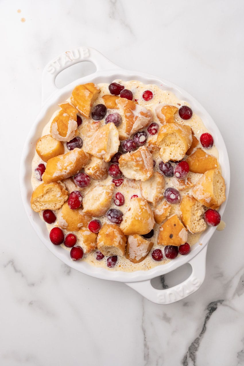 donut pieces and fresh cranberries in custard in a white pie dish