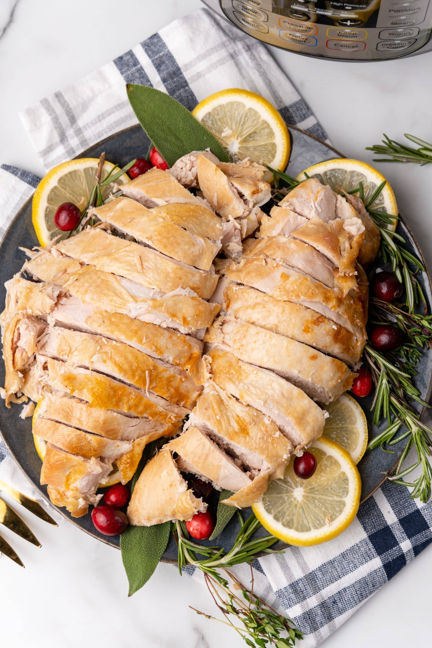 sliced cooked instant pot turkey breast on a bed of fresh herbs and lemon slices