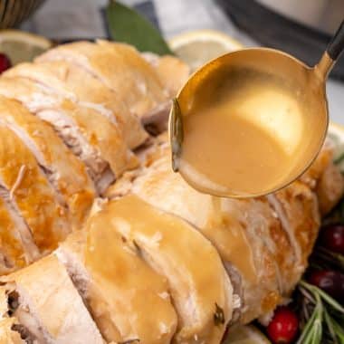 a golden ladle pouring instant pot turkey gravy over sliced turkey breast