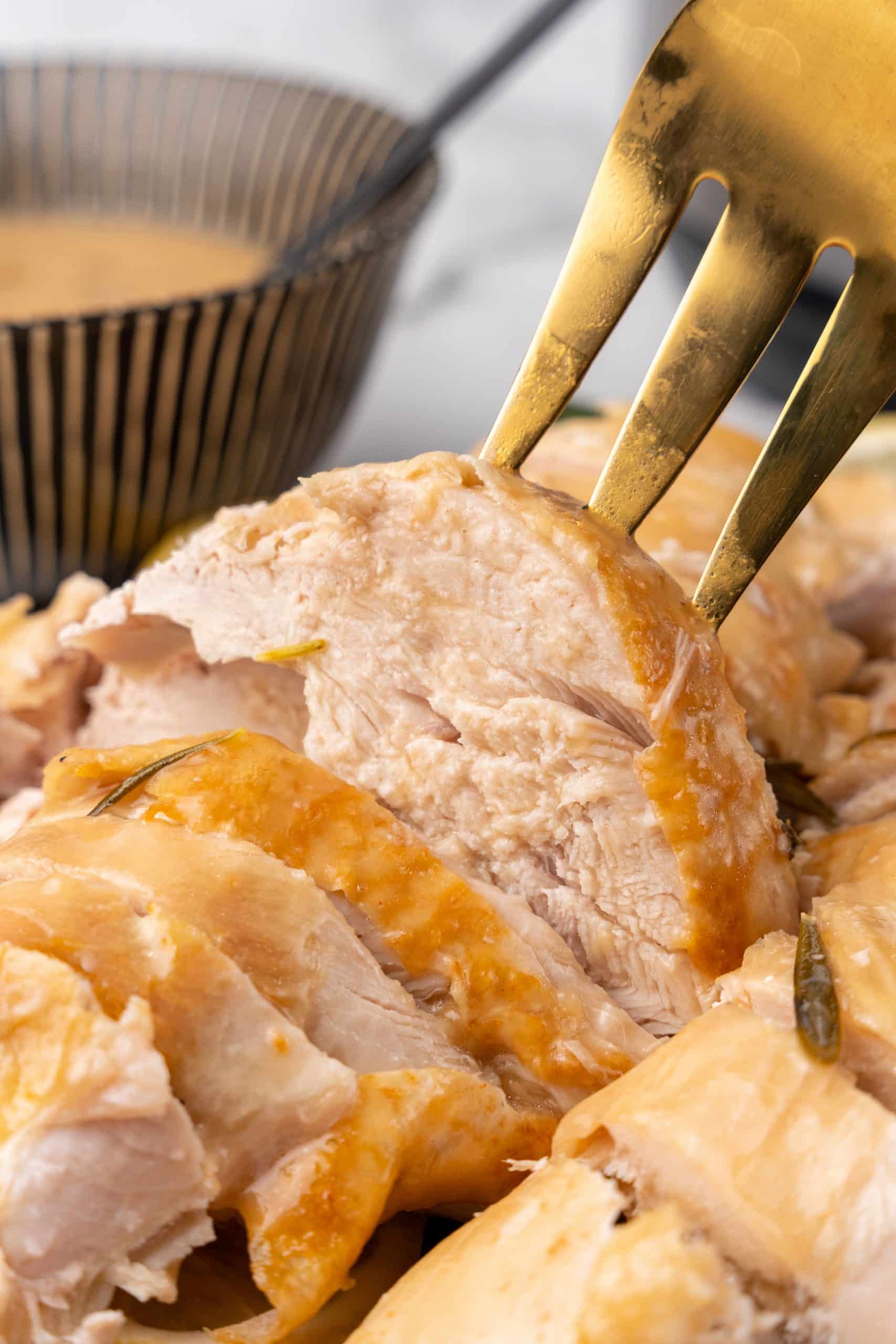 a golden meat fork holding up a slice of instant pot turkey breast