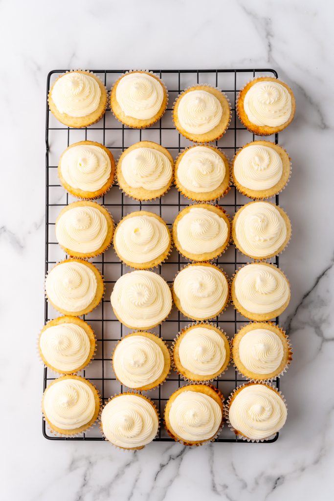 champagne flavored buttercream frosting on vanilla cupcakes on a metal cooling rack