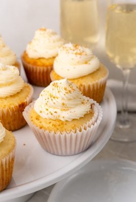champagne cupcakes on a white cake stand in front of flutes of champagne