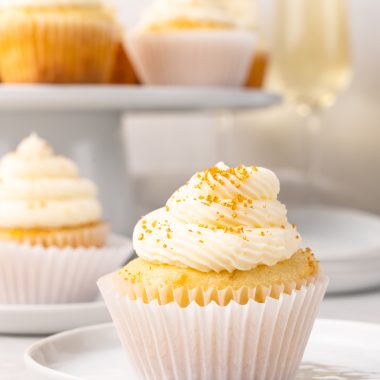 a gold sprinkle topped champagne cupcake on a small white dessert plate
