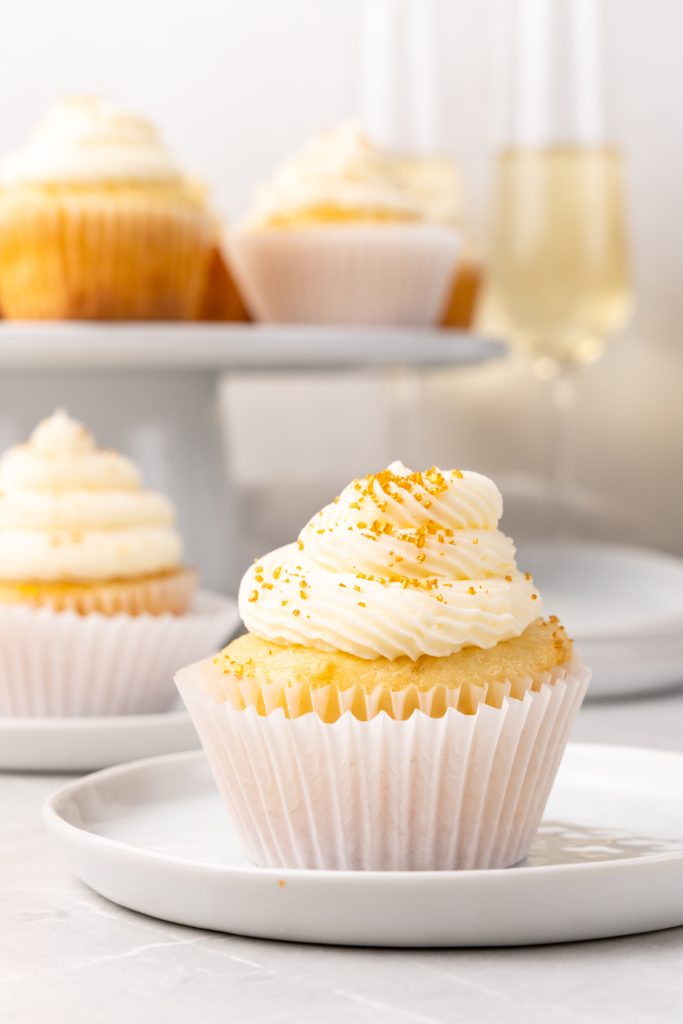 a gold sprinkle topped champagne cupcake on a small white dessert plate