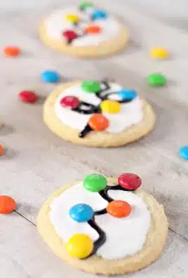 THREE CHRISTMAS LIGHT COOKIES ARRANGED IN A ROW WITH CANDIES IN THE BACKGROUND