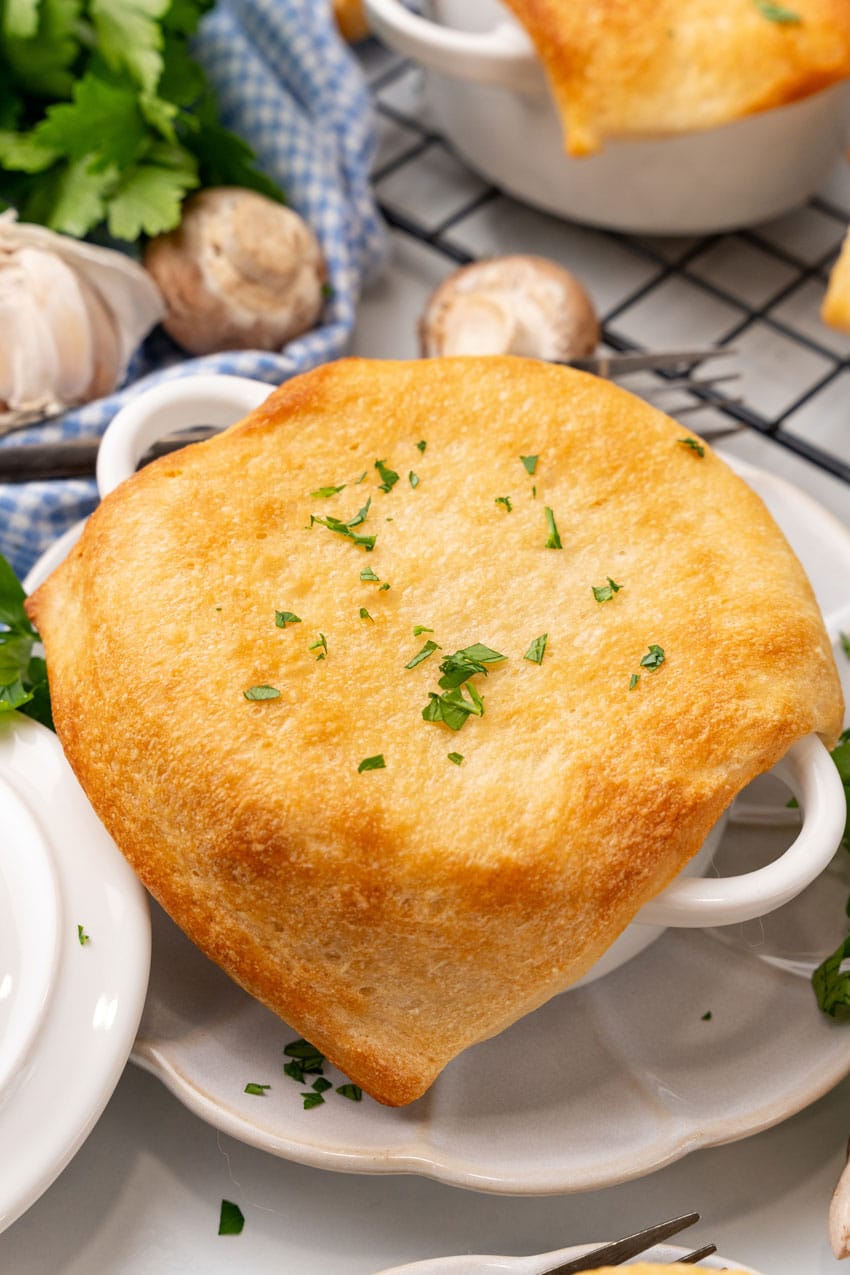 pizza pot pie in a white ramekin on a small white scalloped plate surrounded by fresh herbs