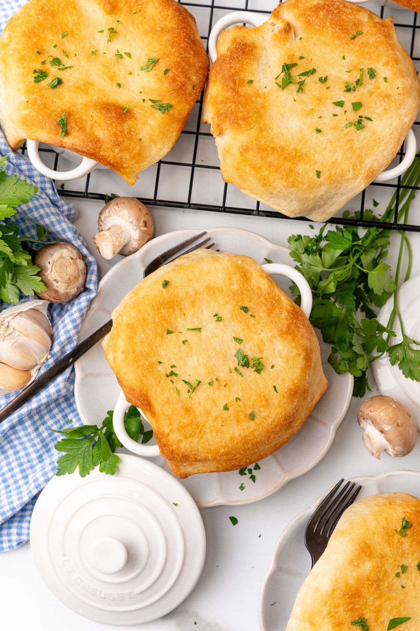 pizza pot pie in a white ramekin on a small white scalloped plate surrounded by fresh herbs