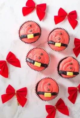 santa belt cupcakes next to red bows on a marbled countertop