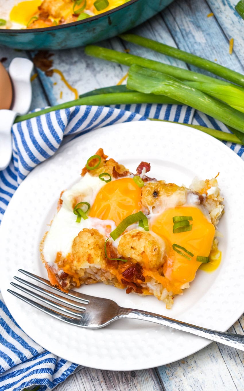 a slice of breakfast totchos on a small white plate with a silver fork on the side