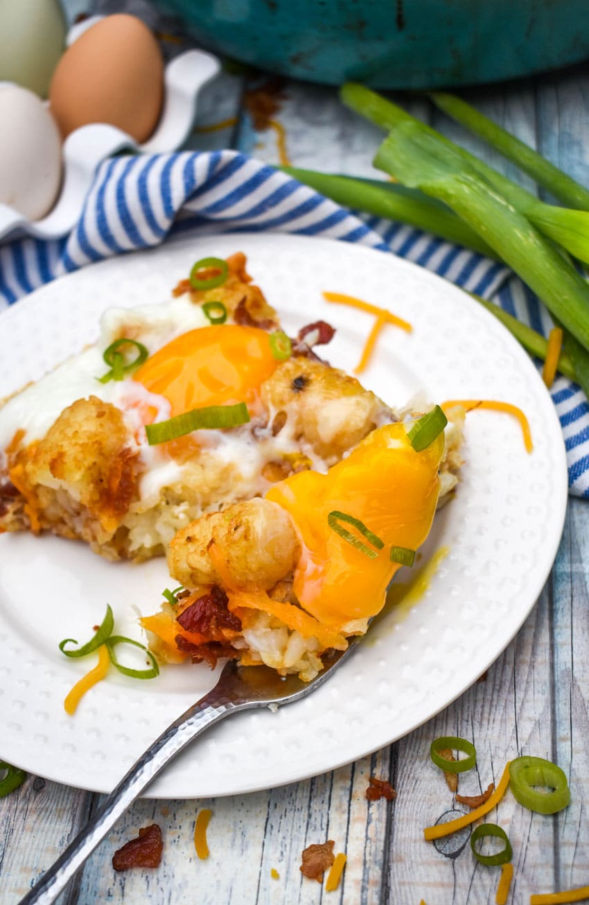 a slice of breakfast totchos on a small white plate with a silver fork on the side