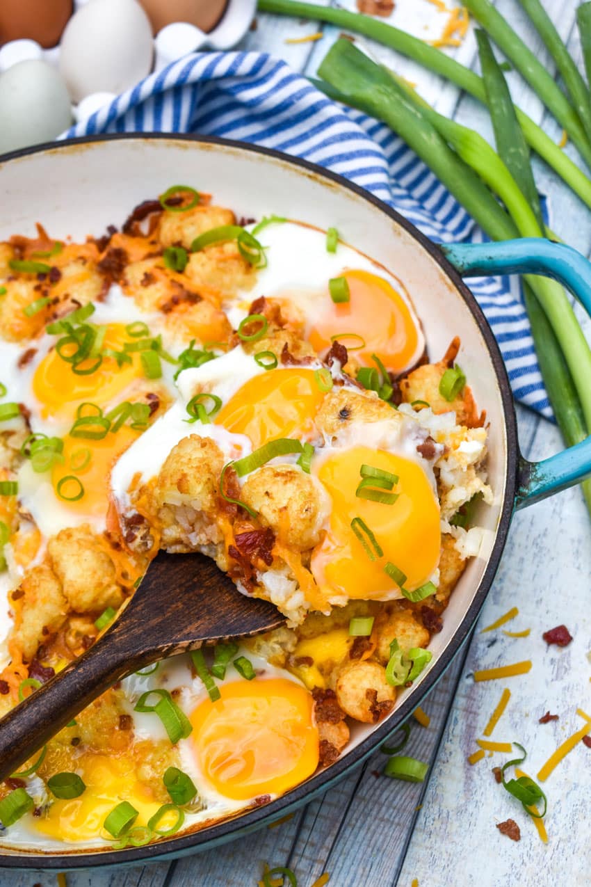 a wooden spatula scooping a slice of breakfast totchos out of a cast iron skillet