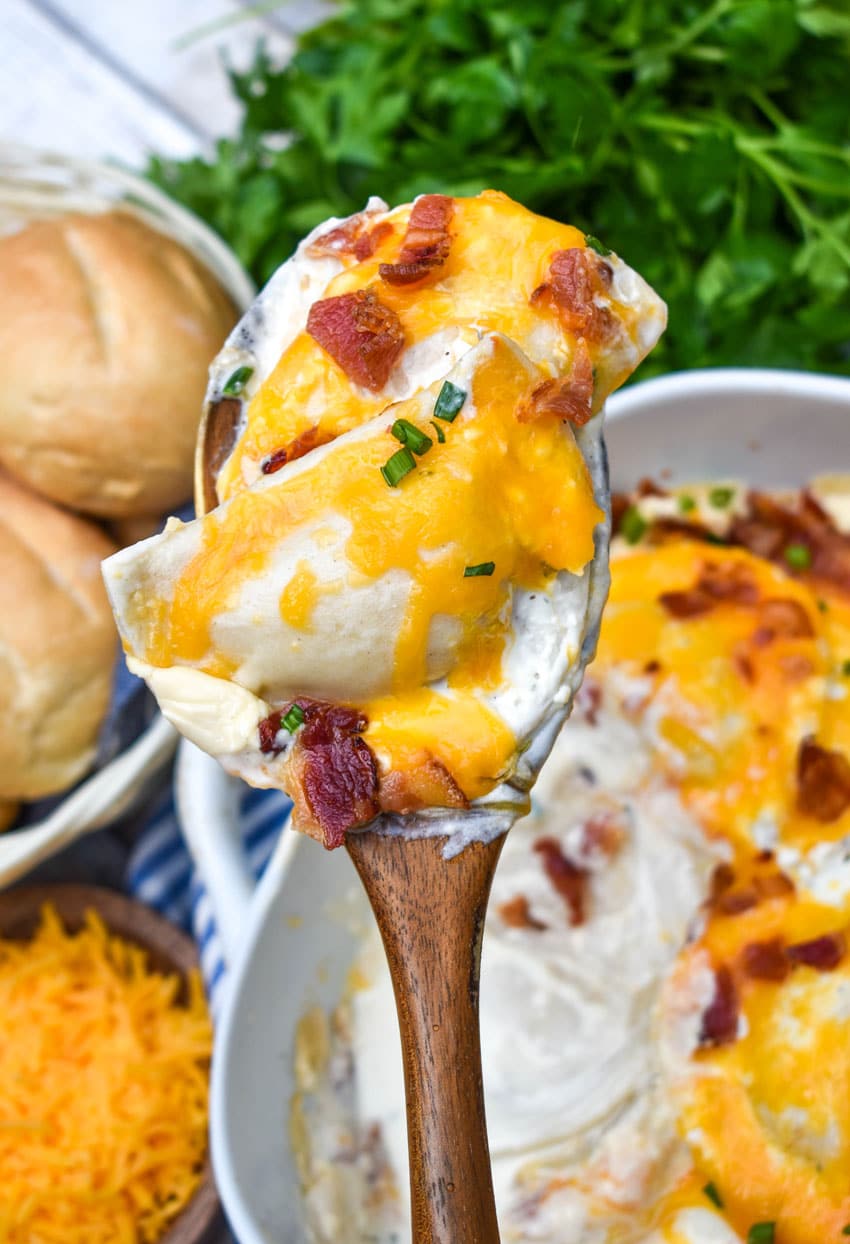 a wooden spoon holding up a scoop of cheddar bacon ranch pierogi bake
