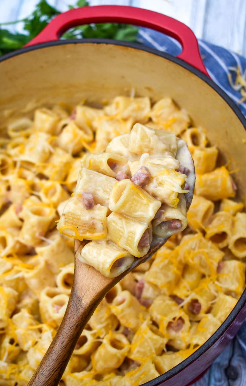 a wooden spoon holding up a scoop of cheesy riggis pasta with ham