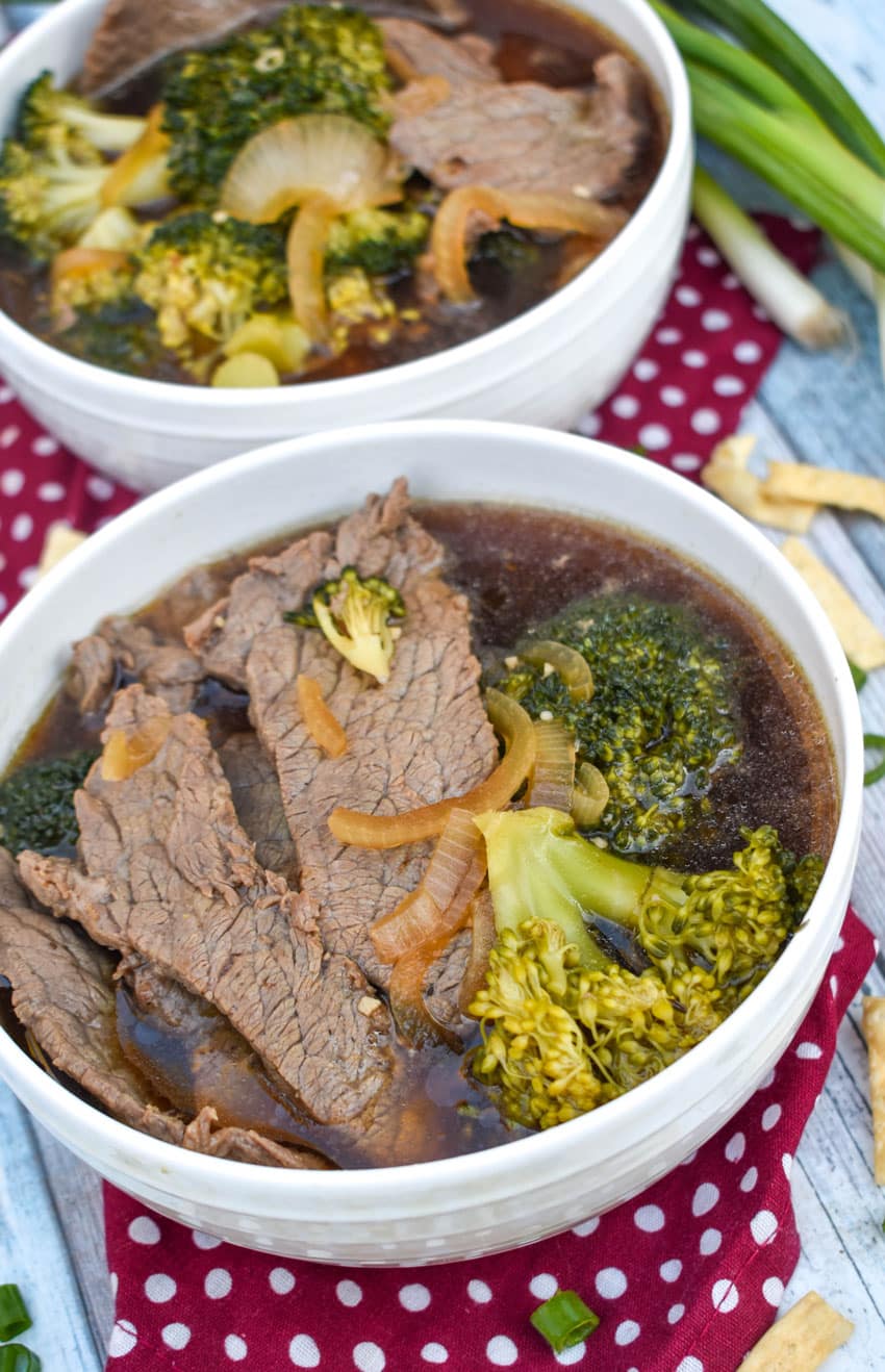 chinese beef and broccoli soup in two white bowls with green onions on the side