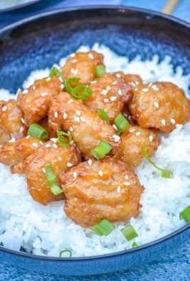 ORANGE CHICKEN TOPPPED WITH SESAME SEEDS AND SLICED GREEN ONIONS OVER COOKED WHITE RICE IN A BLUE BOWL