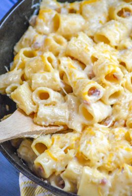 a wooden spoon in a cast iron skillet filled with cheesy riggis pasta with ham