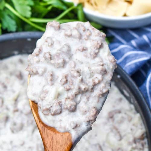a wooden spoon holding up a scoop of country gravy with ground beef