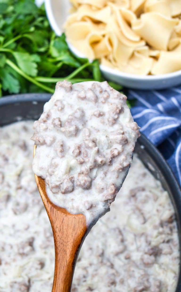 a wooden spoon holding up a scoop of country gravy with ground beef