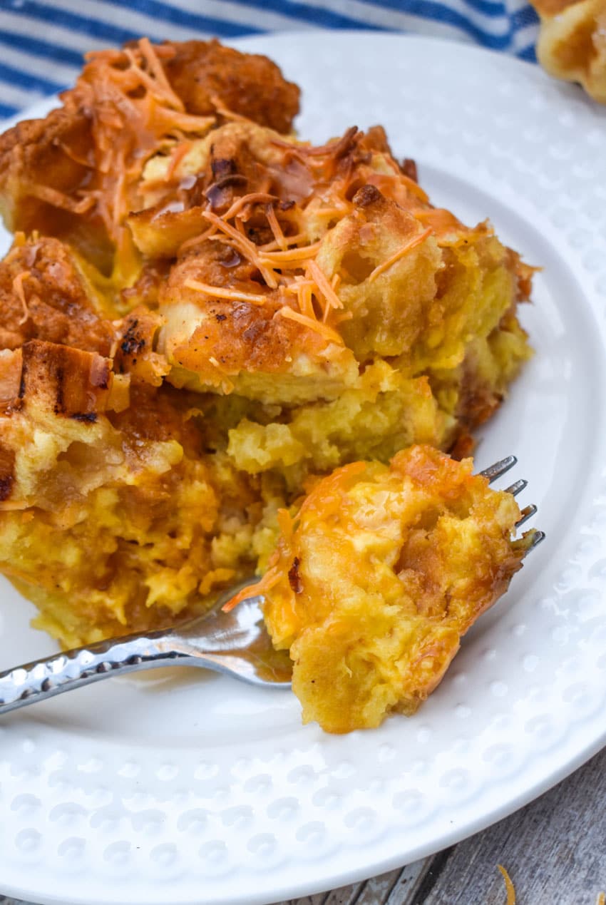 a fork resting on the edge of a small white plate holding a bite of chicken and waffle breakfast bake