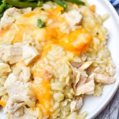 cheesy chicken rice pilaf casserole on a white plate with green beans on the side
