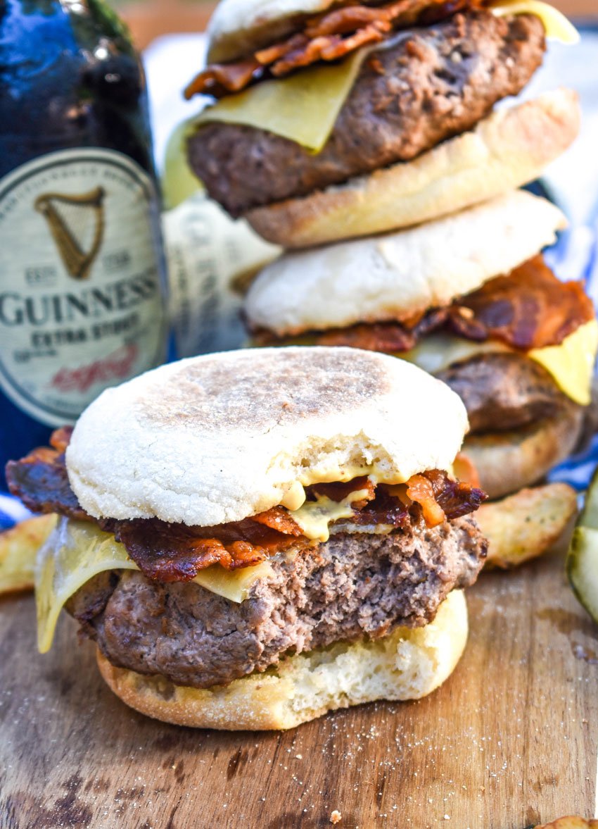 a cheesy guinness burger with a bite out of it sitting on a wooden cutting board