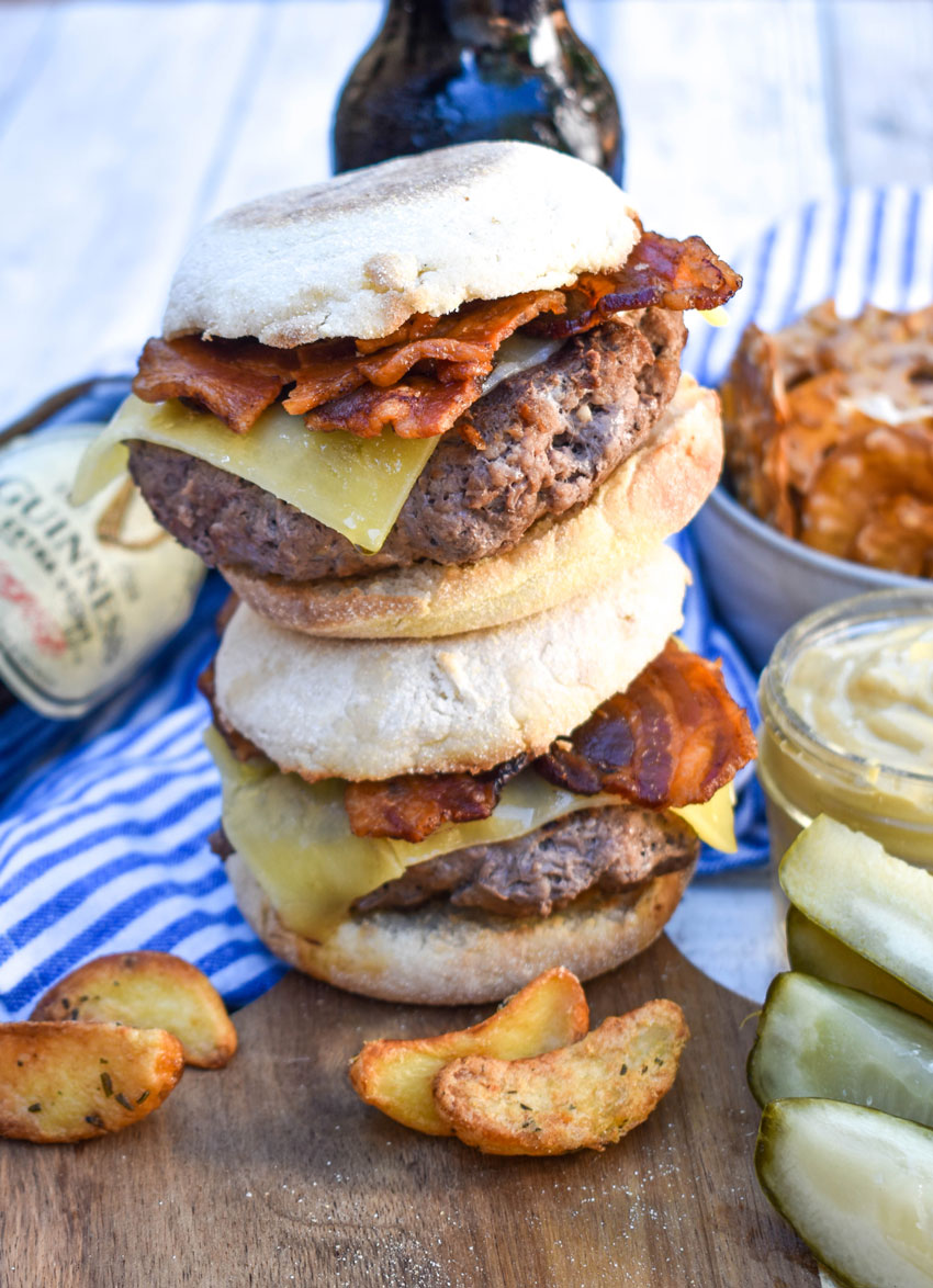 two guinness cheeseburgers on english muffins stacked on top of each other