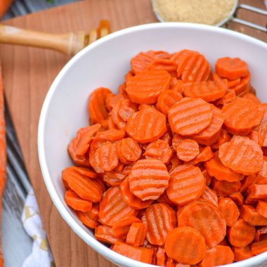 brown sugar honey glazed carrots in a white serving bowl on a wooden cutting board