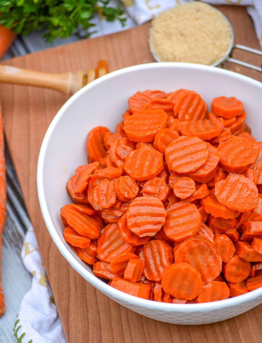 brown sugar honey glazed carrots in a white serving bowl on a wooden cutting board