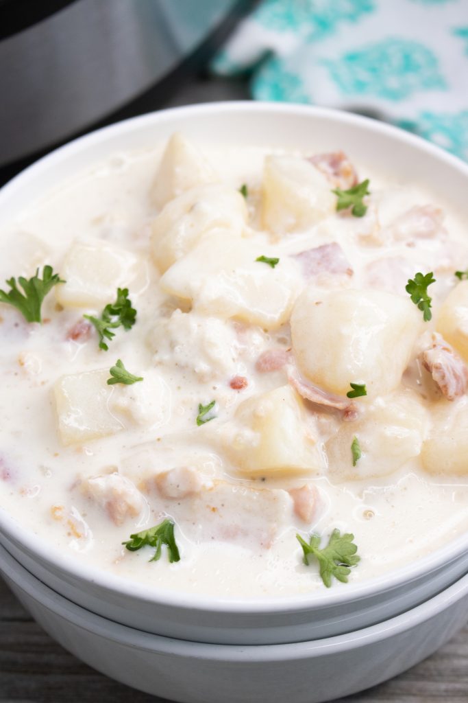 instant pot clam chowder shown in stacked white serving bowl with fresh parsley leaves sprinkled on top with an instant pot in the background