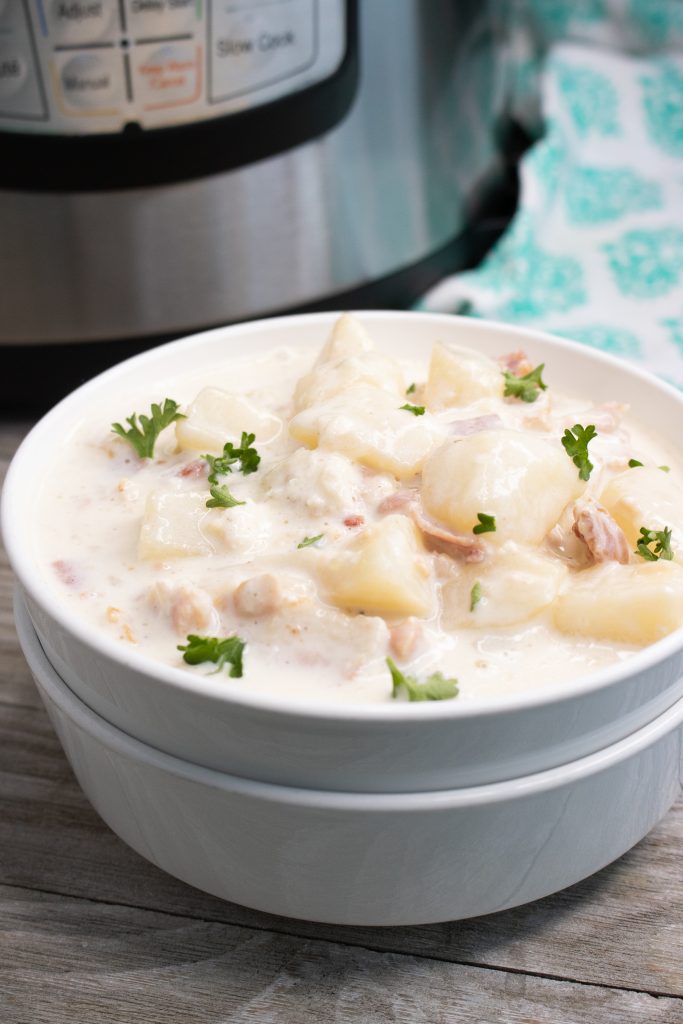 instant pot clam chowder shown in stacked white serving bowl with fresh parsley leaves sprinkled on top with an instant pot in the background