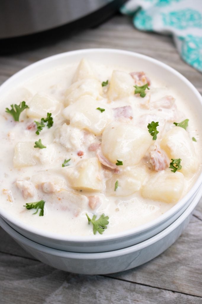 instant pot clam chowder shown in stacked white serving bowl with fresh parsley leaves sprinkled on top