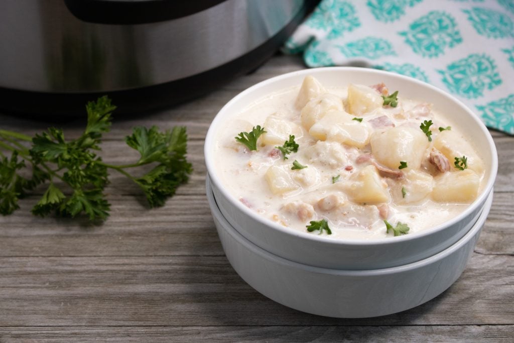 instant pot clam chowder shown in stacked white serving bowl with fresh parsley leaves sprinkled on top with an instant pot in the background