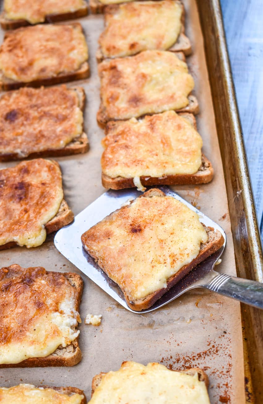 a silver spatula removing a slice of cheesy parmesan rye cocktail bites on a parchment paper lined baking sheet