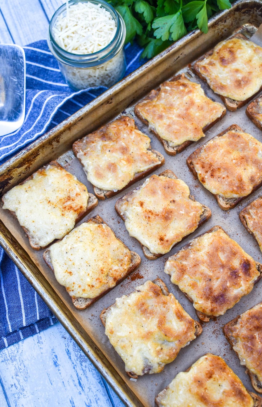 cheesy parmesan rye cocktail bites arranged in rows on a metal baking sheet