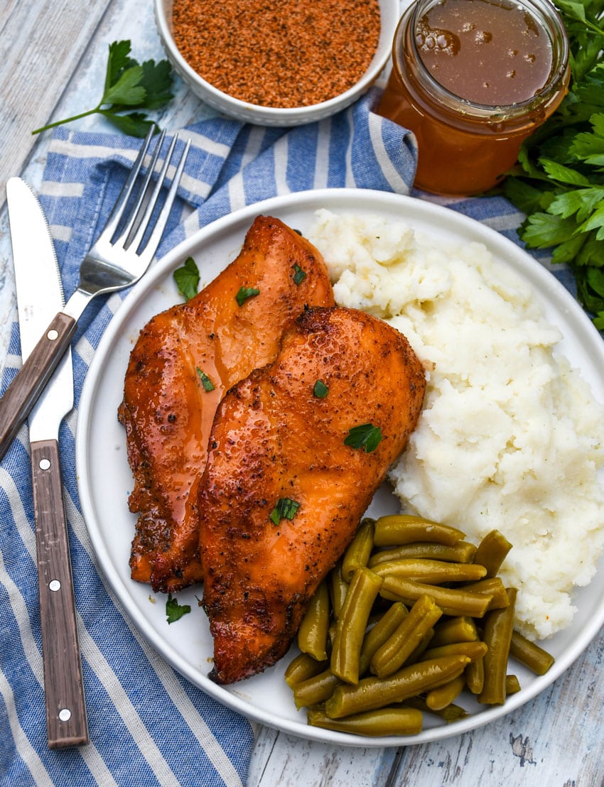 smoked cajun honey chicken breasts next to mashed potatoes and canned green beans on a white plate