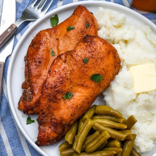 smoked cajun honey chicken breasts next to mashed potatoes and canned green beans on a white plate
