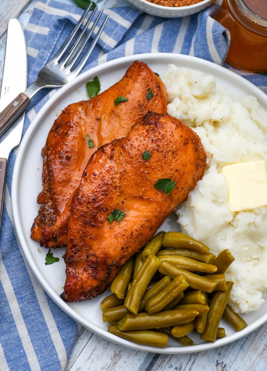 smoked cajun honey chicken breasts next to mashed potatoes and canned green beans on a white plate