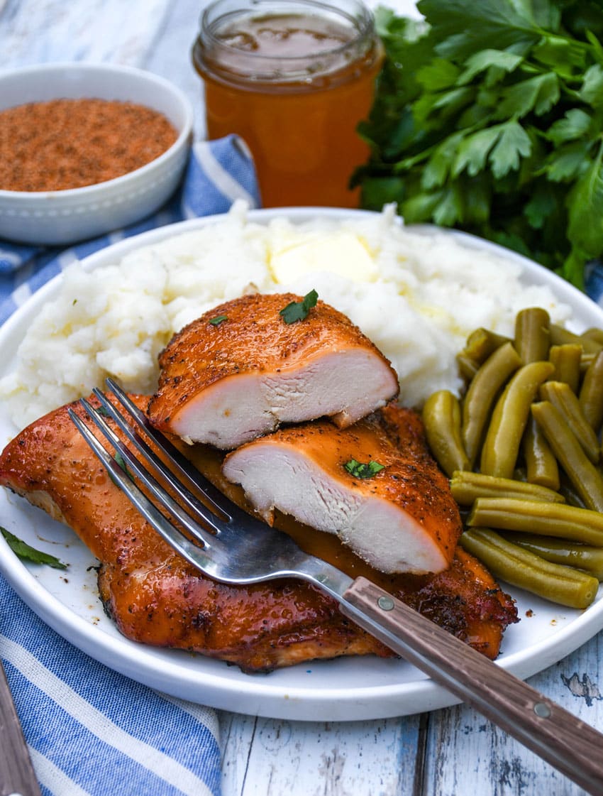 smoked cajun honey chicken breasts next to mashed potatoes and canned green beans on a white plate