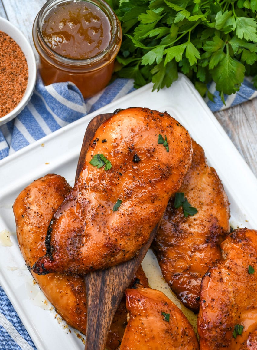 a wooden spatula lifting a smoked Cajun honey chicken breast off a white serving platter