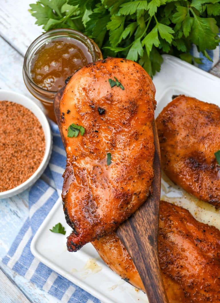 a wooden spatula holding up a smoked cajun honey chicken breast topped with fresh parsley leaves