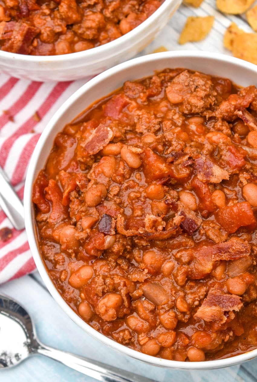 ground beef baked bean chili in a white bowl surrounded by corn chips