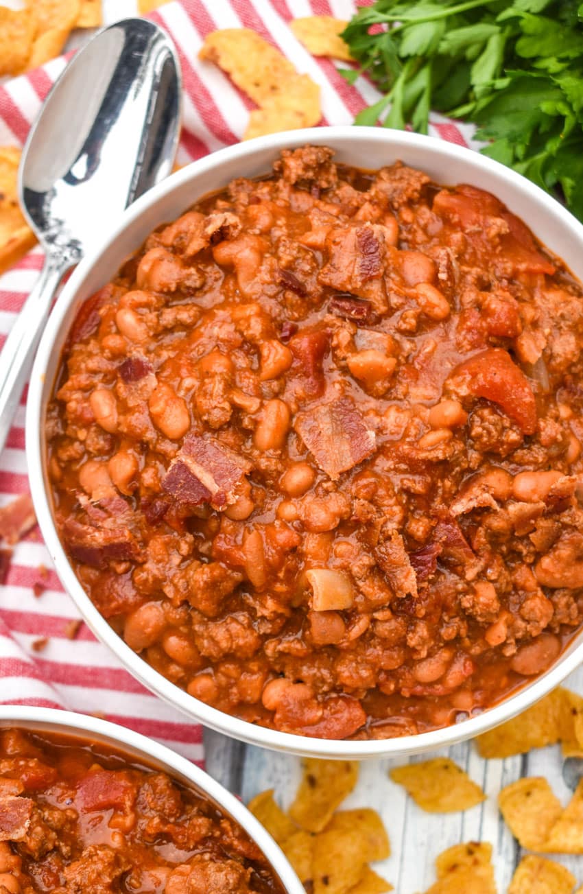 ground beef baked bean chili in a white bowl surrounded with corn chips