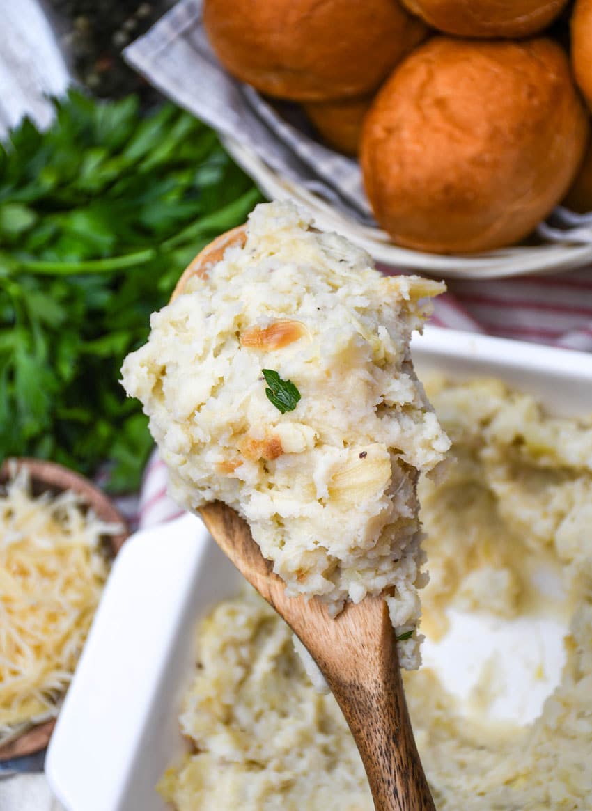 a wooden serving spoon holding up a scoop of creamy roasted garlic mashed potatoes