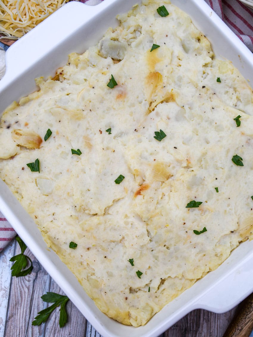 creamy roasted garlic mashed potatoes topped with fresh herbs in a white baking dish