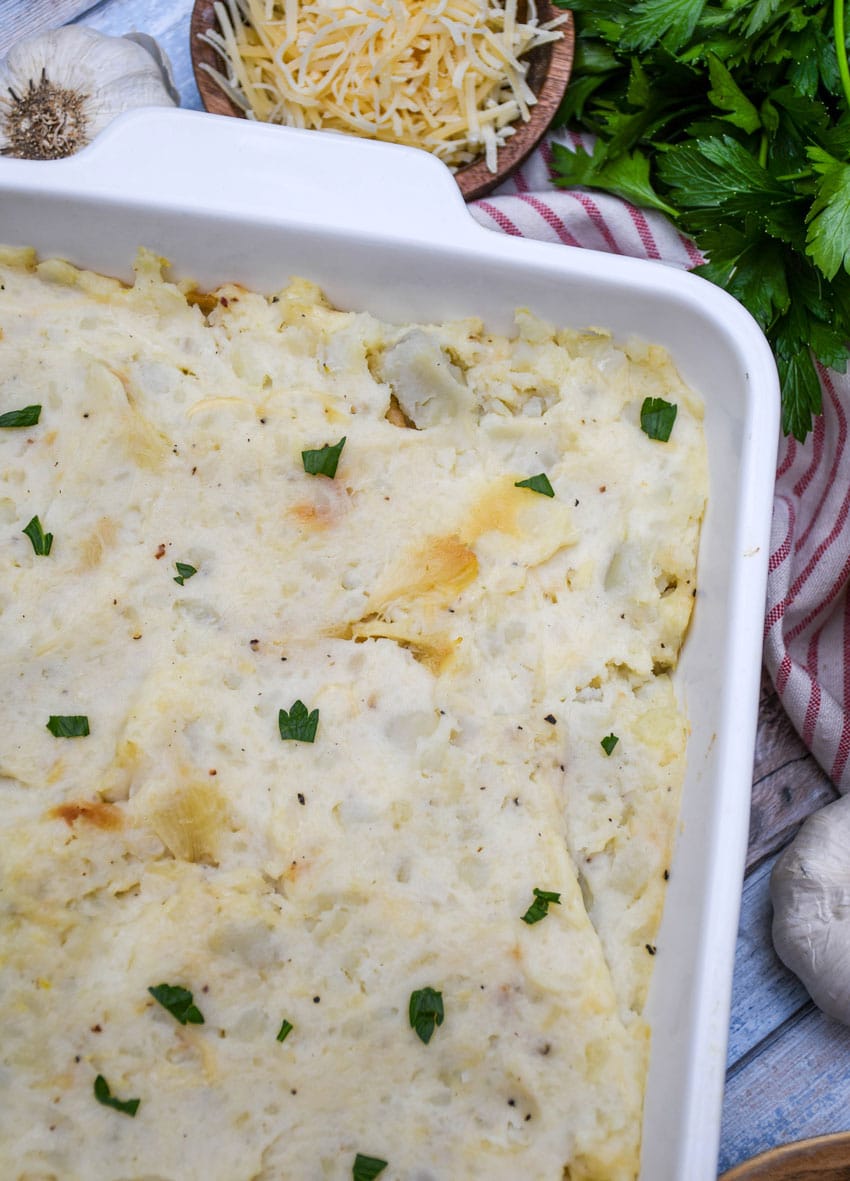 creamy roasted garlic mashed potatoes topped with fresh herbs in a white baking dish