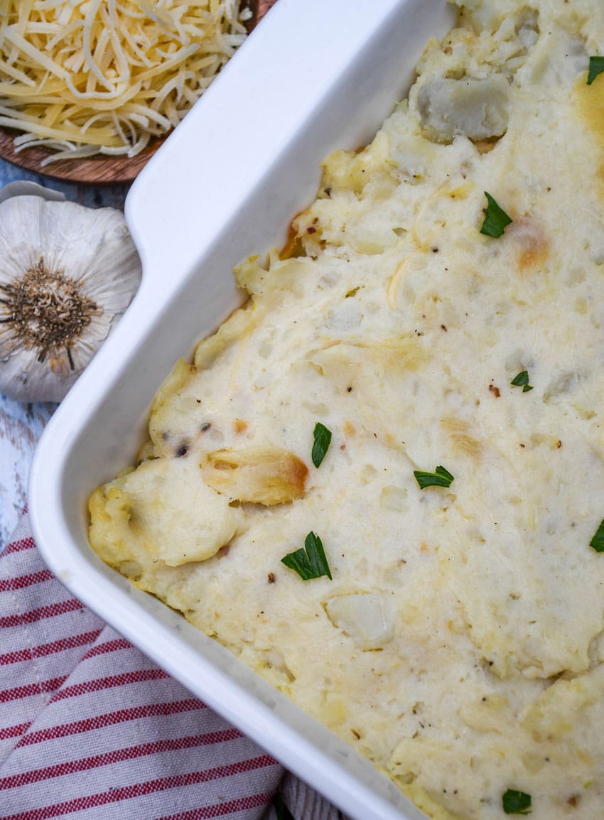 creamy roasted garlic mashed potatoes topped with fresh herbs in a white baking dish