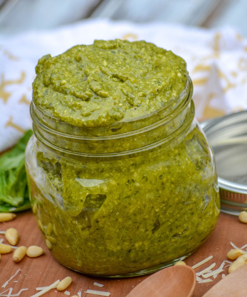 NONNA'S HOMEMADE BASIL PESTO IN A GLASS JAR ON A WOODEN CUTTING BOARD